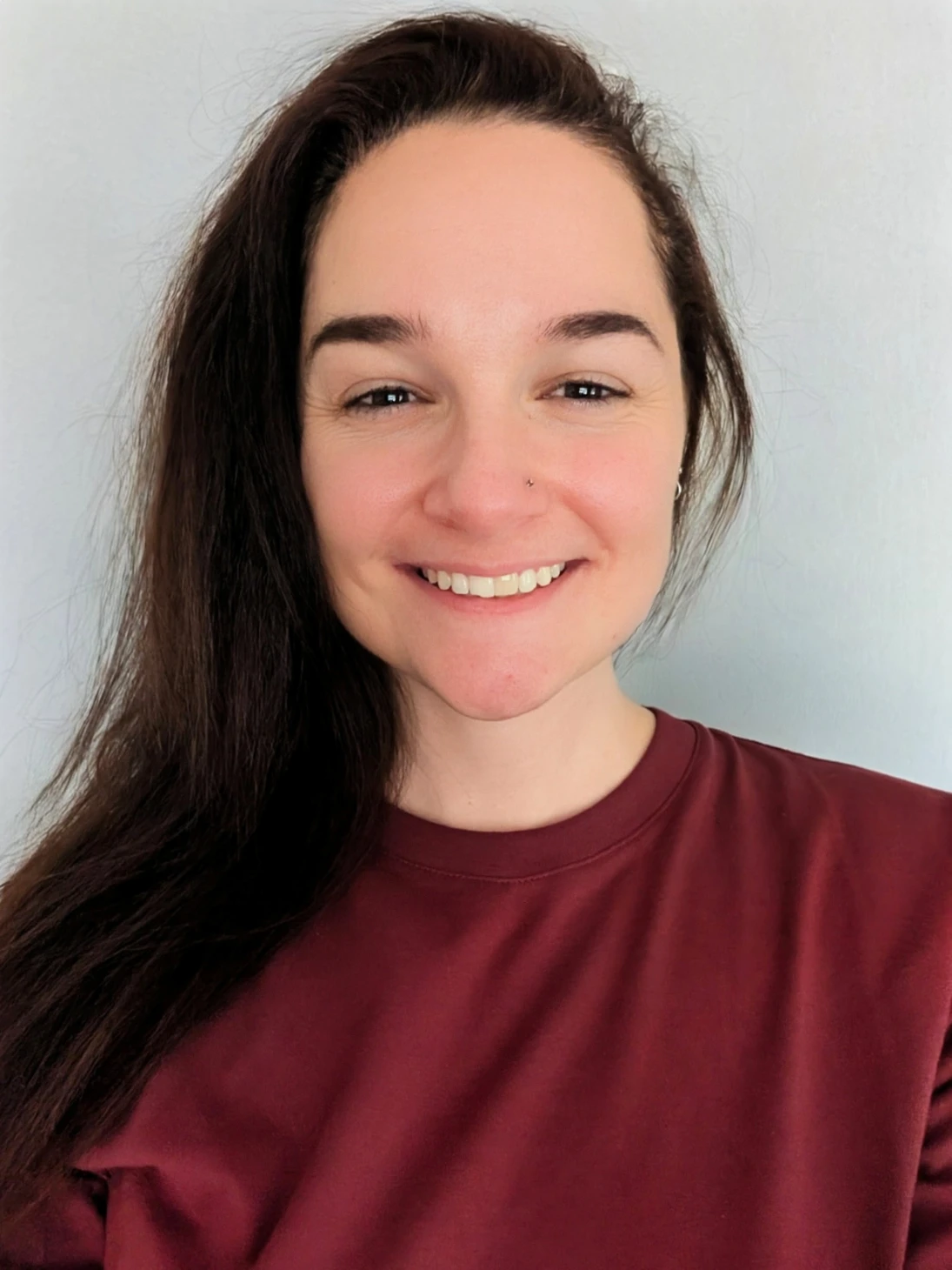 Alana, a Practitioners member at Akashahealth with long dark hair and maroon shirt, smiles at camera, light background.