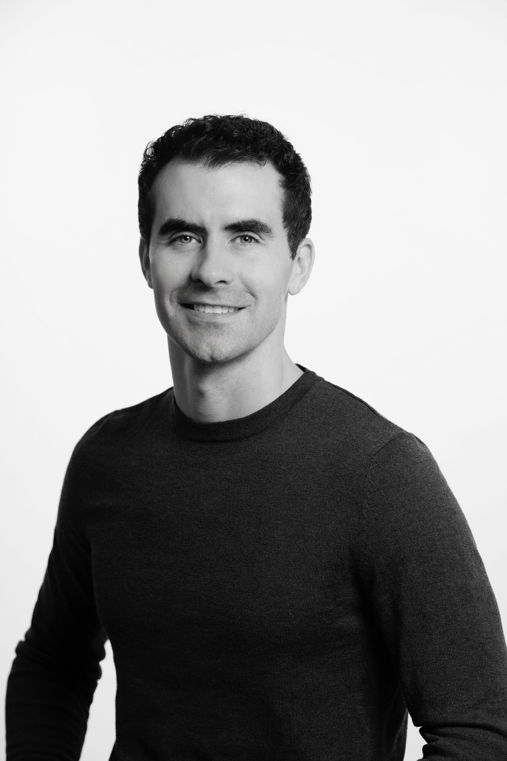 Dr. Derek, Practitioner at Akashahealth, with short curly hair, smiles in a dark shirt against a plain white background.