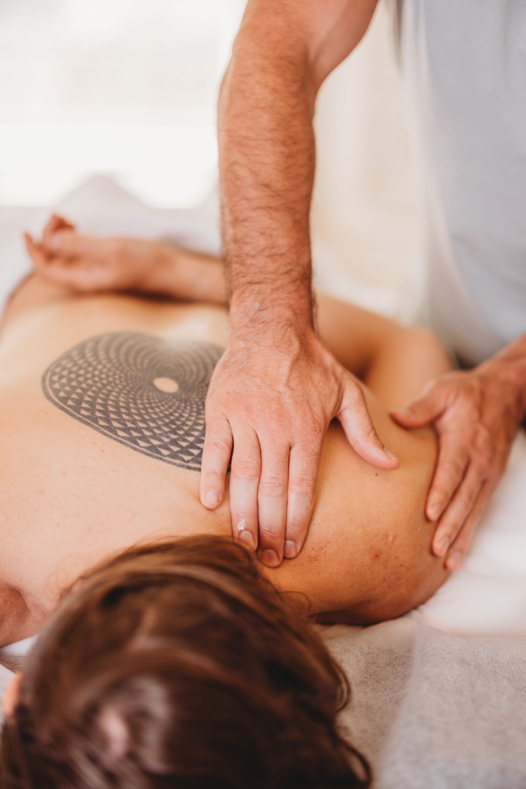 Akasha Health back massage session; one arm bent to reveal a large circular tattoo on the upper back.